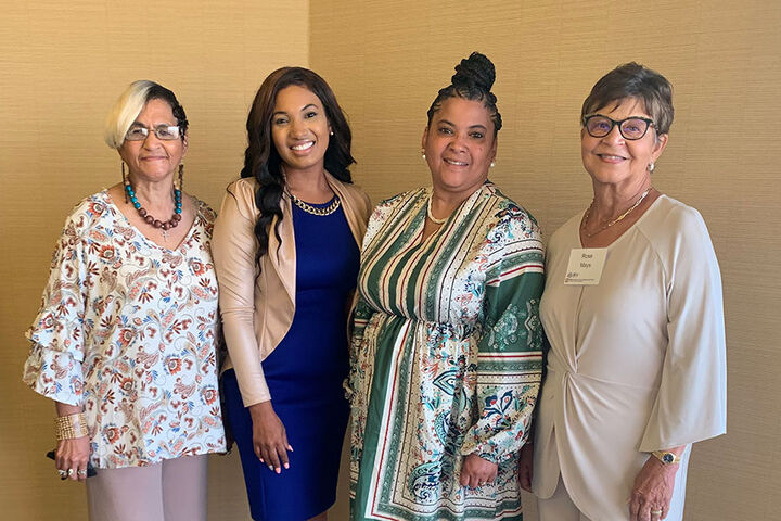 Four women stand together, smiling.